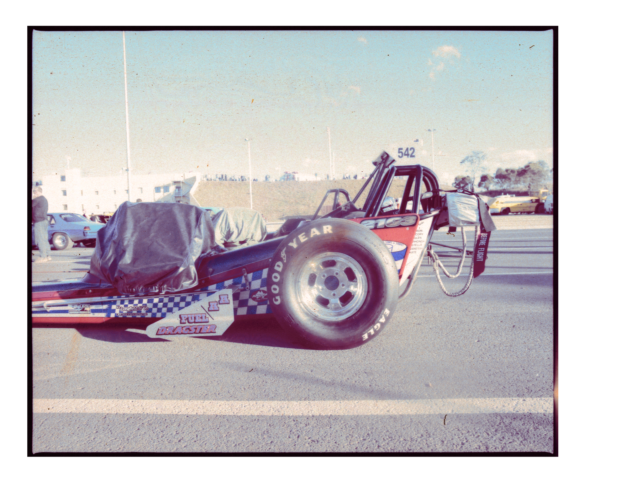 Drag racing car with a black tarp covering part of the vehicle on an asphalt race track. Good Year and Eagle logos are visible.