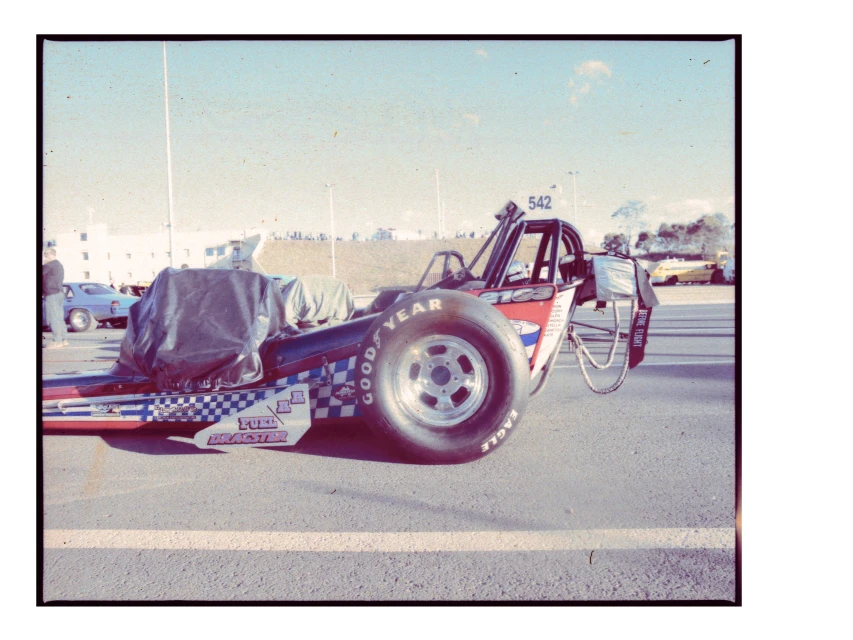 Drag racing car with a black tarp covering part of the vehicle on an asphalt race track. Good Year and Eagle logos are visible.