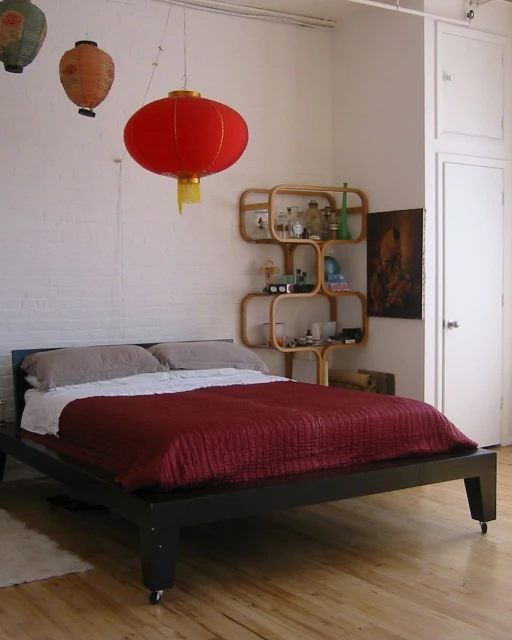 Bedroom interior with a black platform bed, red blanket, and hanging Chinese lanterns providing soft, ambient lighting in the room.