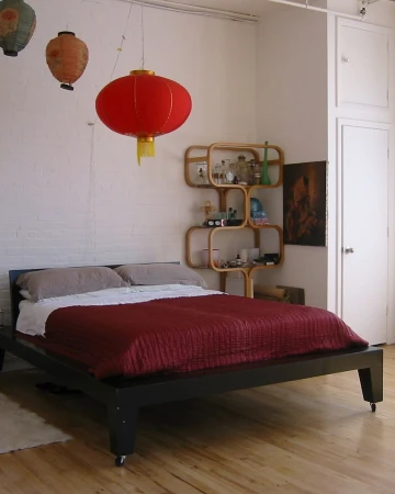 Bedroom interior with a black platform bed, red blanket, and hanging Chinese lanterns providing soft, ambient lighting in the room.