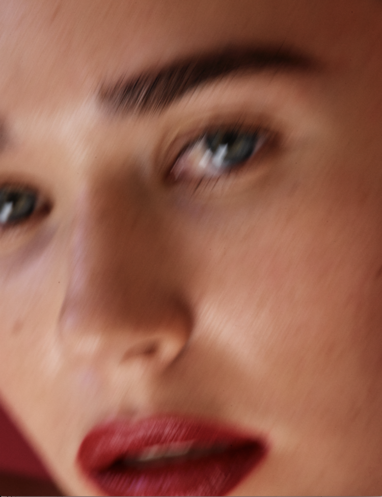Close-up studio shot of a young woman with blue eyes and red lipstick, showcasing beauty, fashion, and cosmetic details in soft lighting.