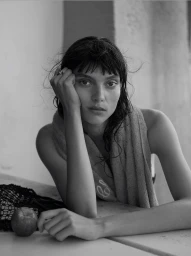 Monochrome portrait of a woman resting her head on her hand with a towel over her shoulder and an apple on the table.