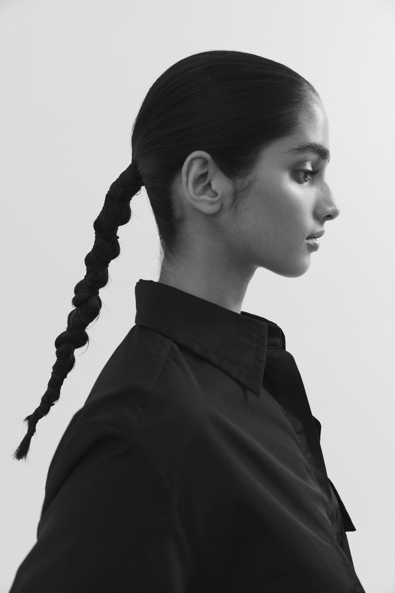 Profile shot of an adult female with her hair in a twisted braid wearing a collared black shirt against a solid white background.