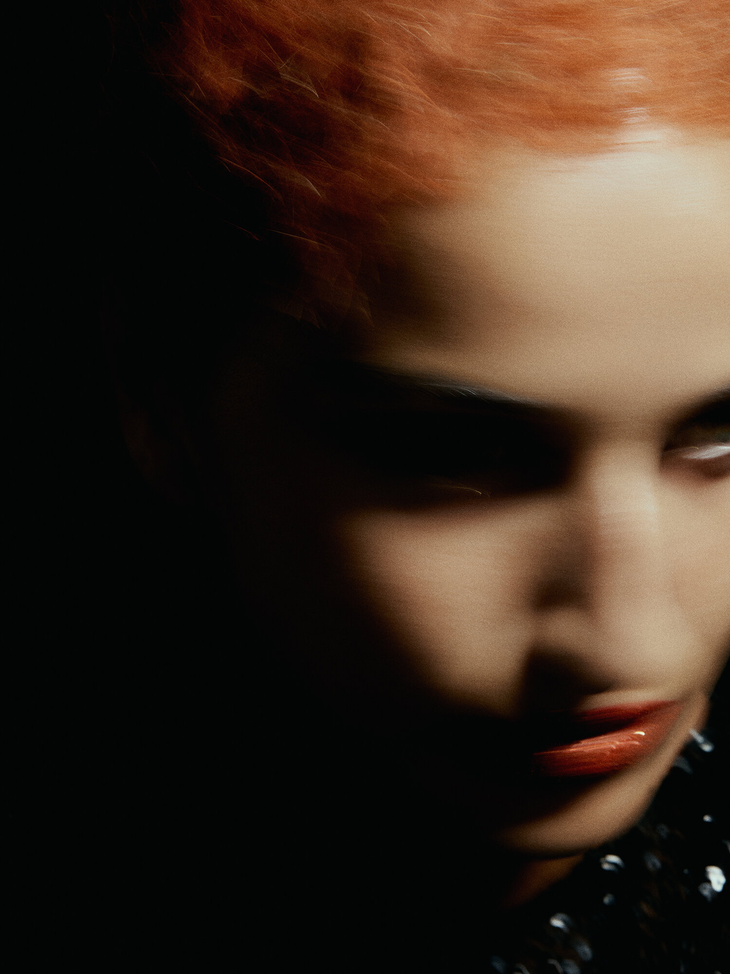 Abstract beauty portrait features a partially visible adult woman with vivid orange hair and glossy red lips against a dark background.