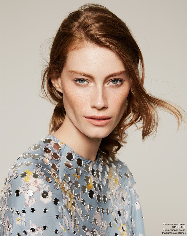 Close-up portrait of a red-haired woman with fair skin, wearing a light blue dress adorned with silver and floral embellishments.