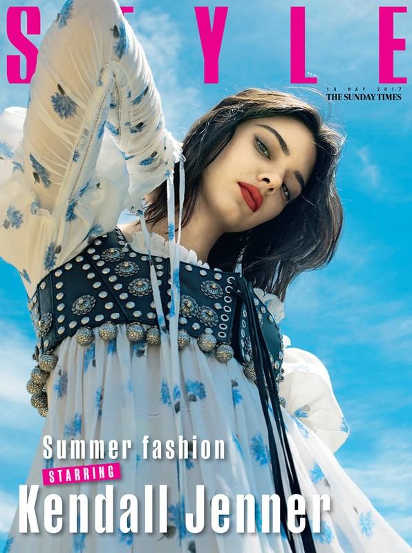 Kendall Jenner on magazine cover posing outdoors in a floral dress with a studded vest and the blue sky as background.