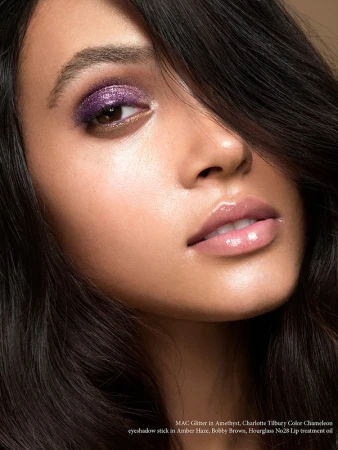 Close-up studio shot of an adult woman with purple glitter eyeshadow and glossy lips, showcasing beauty and fashion makeup.
