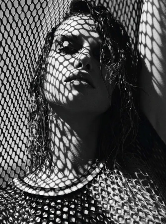 Monochrome portrait of a woman with wet hair under heavy patterned shadows from a mesh screen