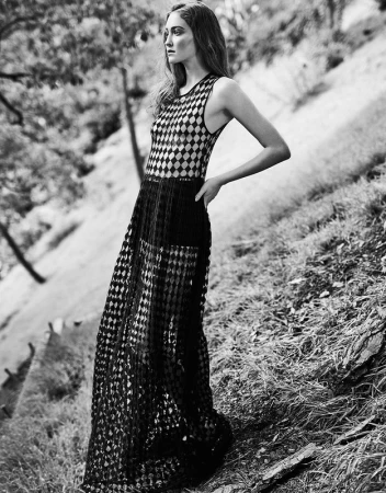 Model in patterned sleeveless maxi dress posing outdoors on a sloping hill with dry grass and trees.