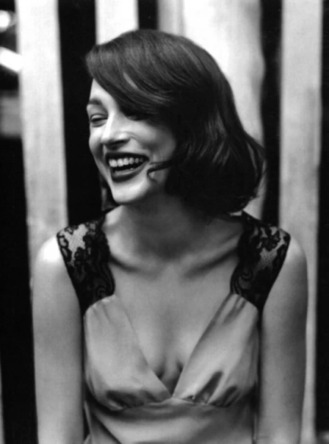 Smiling woman with lace-trimmed dress against black and white striped backdrop in a portrait-style photograph, showcasing a happy expression.