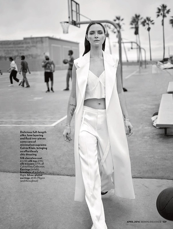 Monochrome fashion shot of a woman in a white silk outfit on a basketball court, surrounded by palm trees and blurry background figures.
