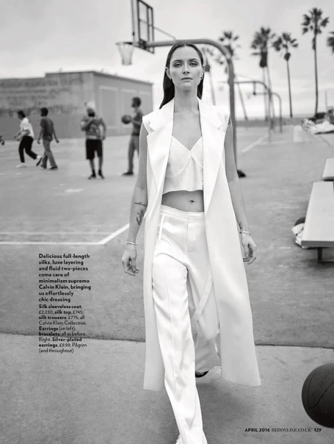 Monochrome fashion shot of a woman in a white silk outfit on a basketball court, surrounded by palm trees and blurry background figures.