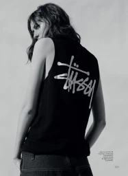 Woman wearing a black sleeveless shirt with a Stussy logo on the back, looking back over her shoulder.