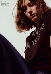 Portrait of a woman with short wavy hair wearing a black graphic t-shirt against a bright background