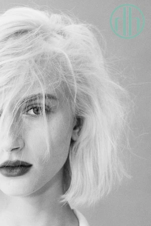 Close-up portrait of a woman with blonde hair across her face and dark lipstick against a neutral background