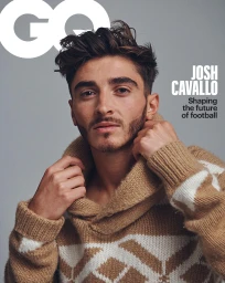 Josh Cavallo wearing a patterned camel and white knitted sweater against a plain grey studio background with magazine cover typography.