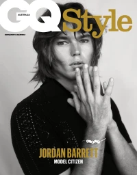 Close-up black and white portrait of male model Jordan Barrett with hands clasped near his face against a plain background.