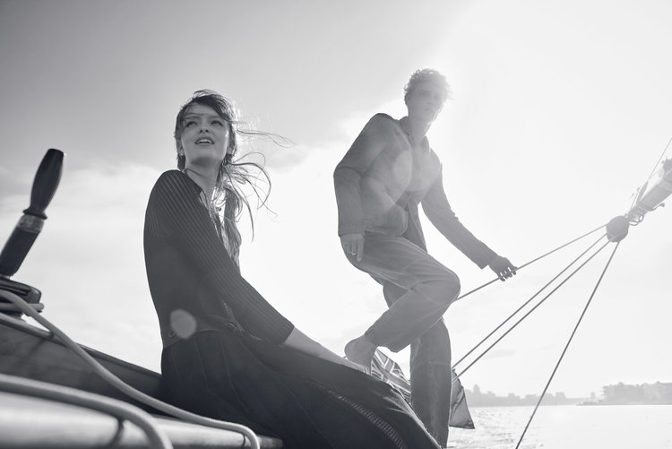 Black and white photo of a fashionable adult woman and man sailing on a boat, with bright sunlight and clear sky.