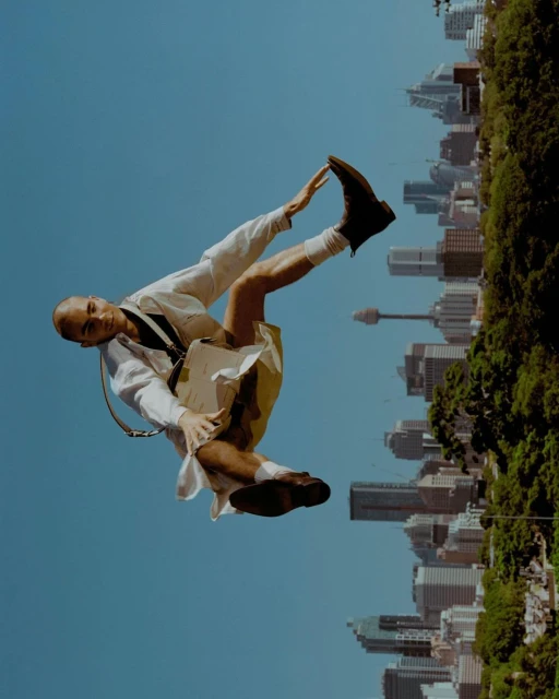 Unique perspective shows a bald man in mid-air against a city backdrop, creating an unexpected juxtaposition of style and urban landscape.