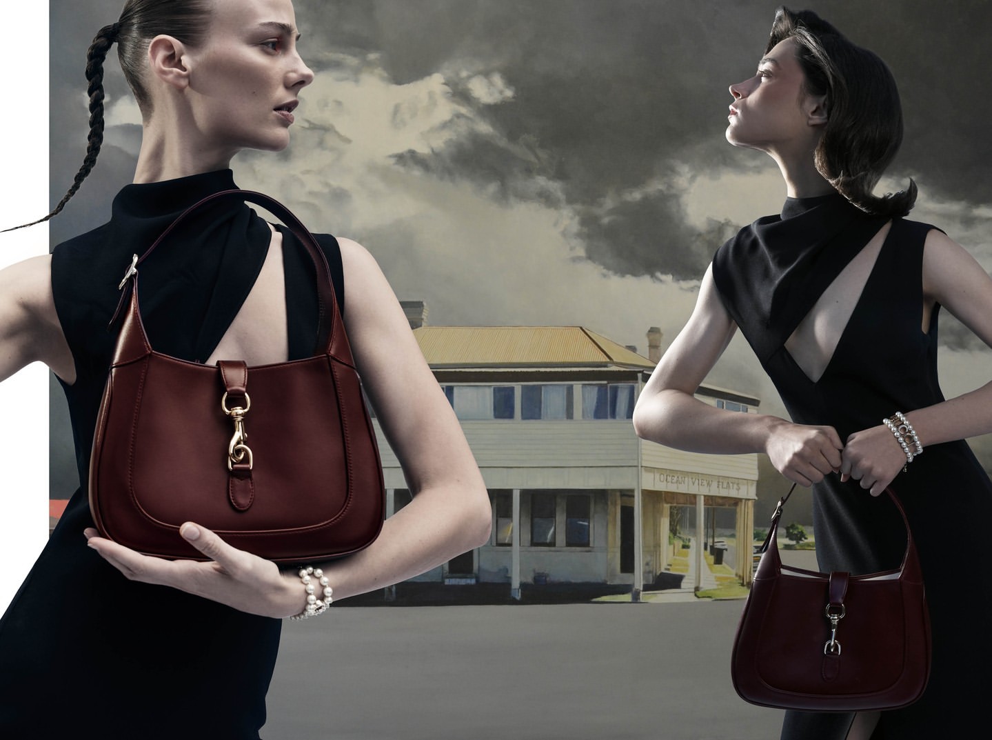 Fashion shot featuring two adult women in black dresses holding brown leather handbags with a building and cloudy sky background.