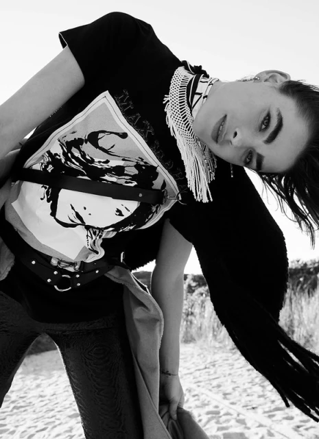Monochrome fashion shot of a woman in printed t-shirt and scarf outdoors, striking a pose on sand under bright daylight.