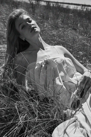 Black and white portrait of a blonde woman lying in tall grass outdoors, captured by Ben Watts.