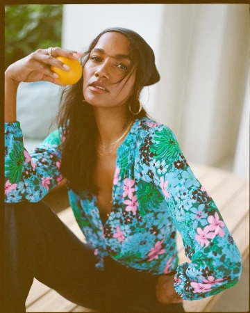 Woman wearing a floral blouse and holding an orange, photographed by Ben Watts.