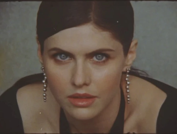 Close-up portrait of a Caucasian woman with dark hair and light eyes, wearing dangling earrings, against a muted background.