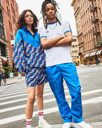 A woman and a man posing together on an urban street, wearing sporty apparel including a blue patterned jacket and shorts and blue track pants.