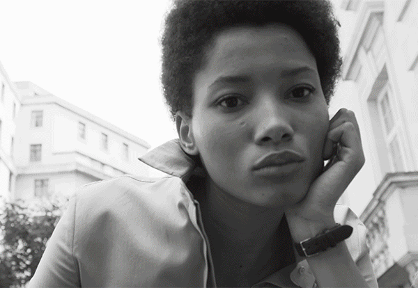 Close-up black and white portrait of a Black woman resting her chin on her hand against an architectural background