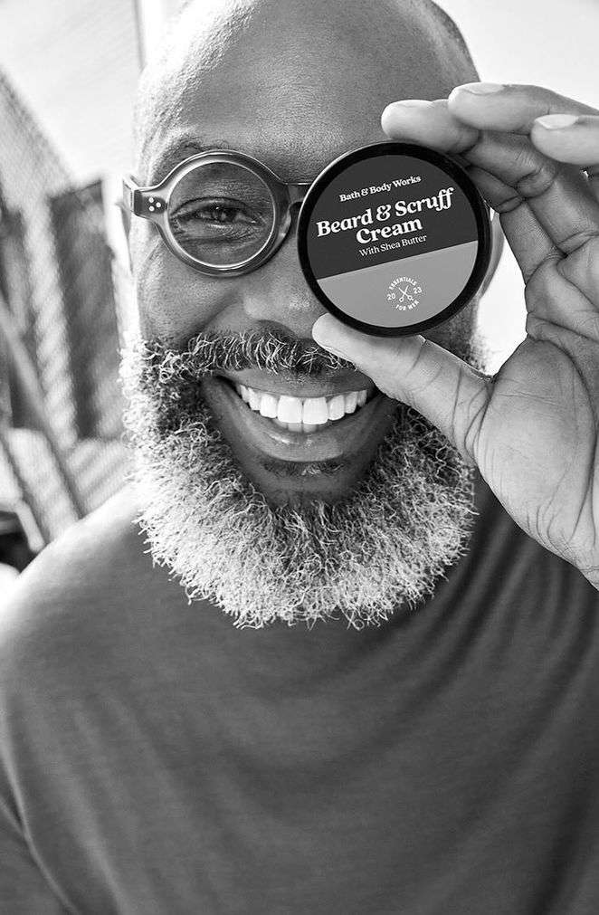 Black and white portrait of a smiling, bearded man with glasses holding a beard cream container, beauty and personal care promotion.