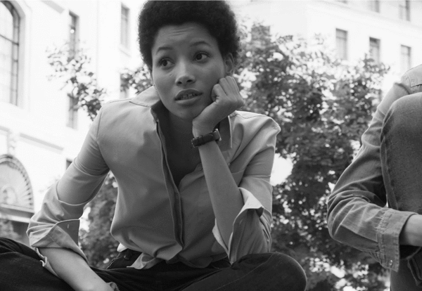 Black and white portrait of a young woman resting her chin on her hand outdoors against an architectural background