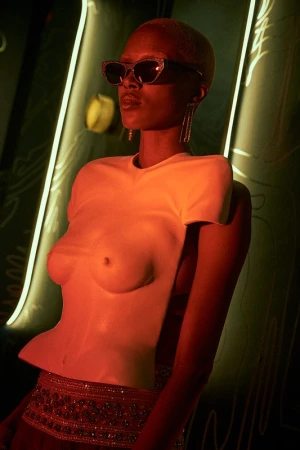 Glamorous short-haired African American woman in stylish sunglasses poses in front of a neon light with a decorative shirt.