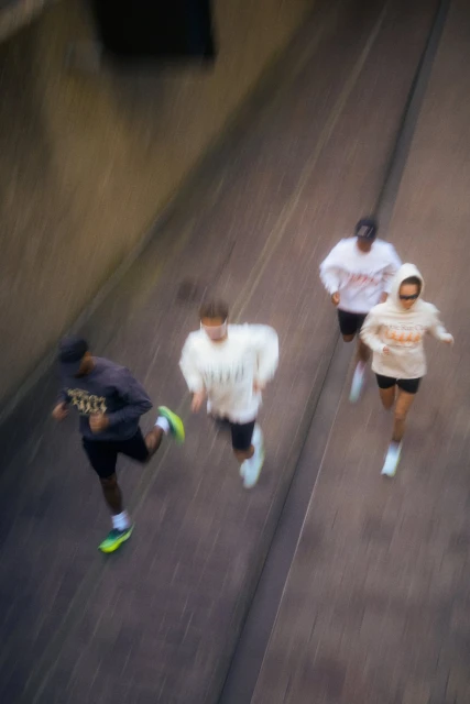 Aerial view of four people running on a paved surface, wearing athletic apparel and shoes, under natural lighting.