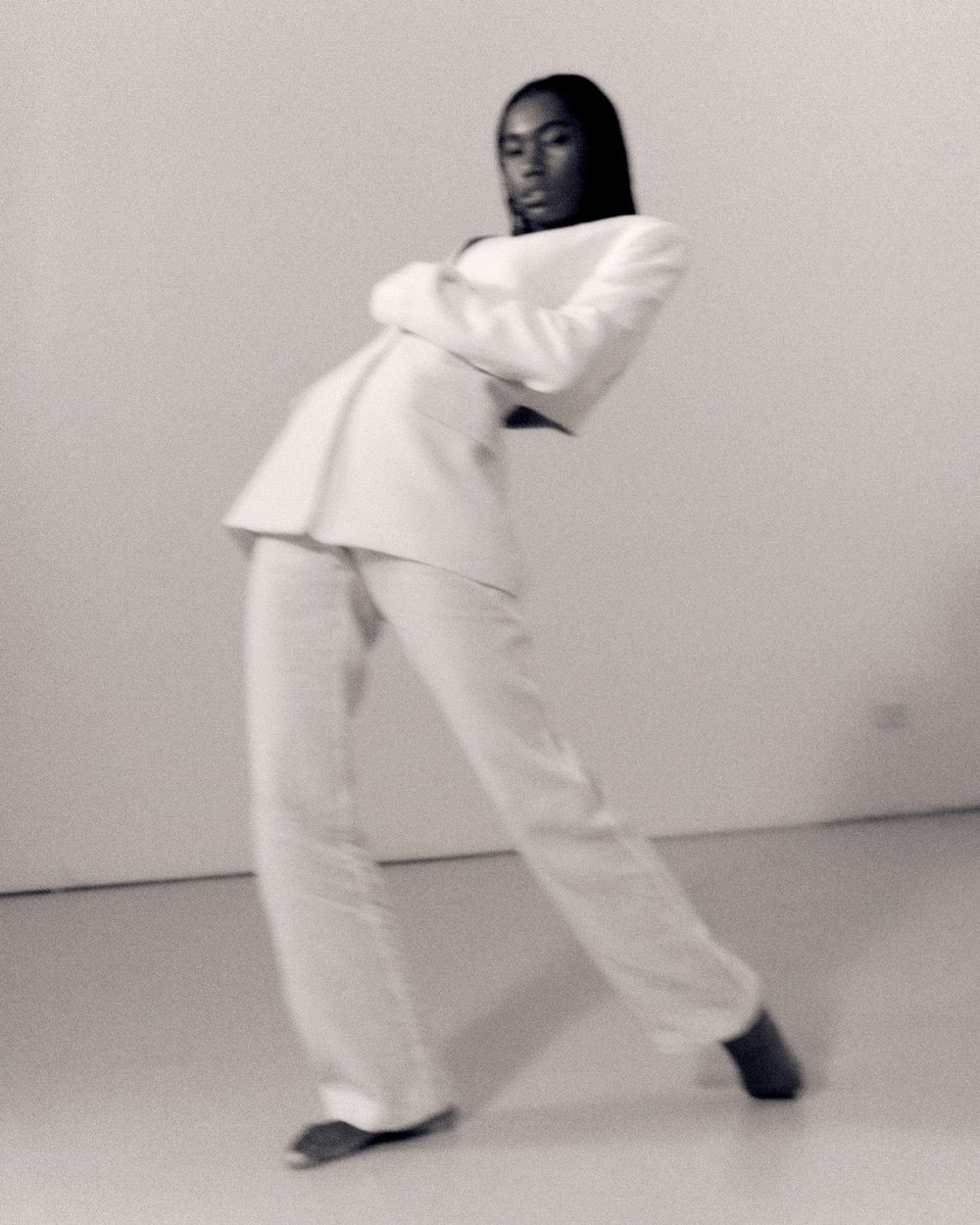 Black woman in a white suit leaning backward against a plain light background