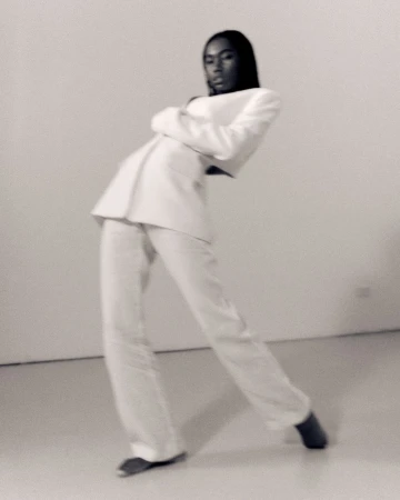 Black woman in a white suit leaning backward against a plain light background