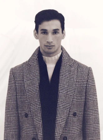 Portrait of a man wearing a plaid double-breasted coat and turtleneck sweater against a light seamless background.