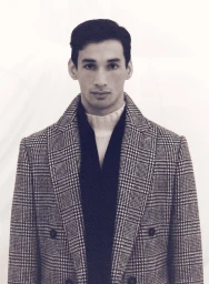 Portrait of a man wearing a plaid double-breasted coat and turtleneck sweater against a light seamless background.