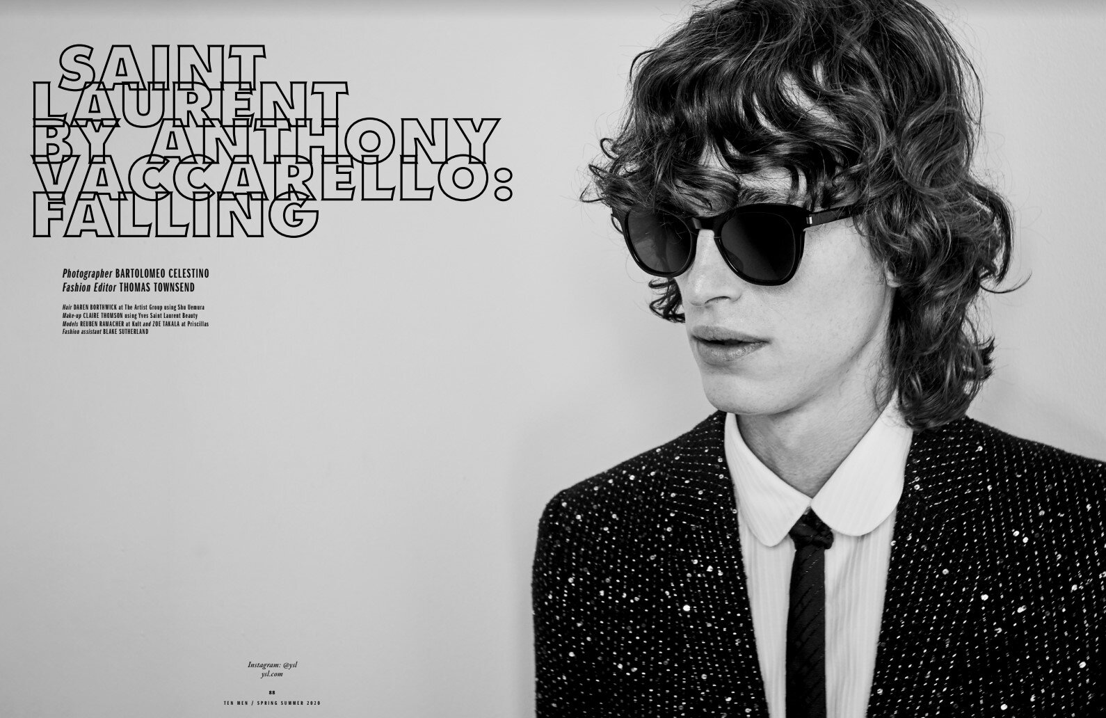 Black-and-white fashion portrait of a young adult male model wearing sunglasses, a patterned jacket, and a white collared shirt with a tie.