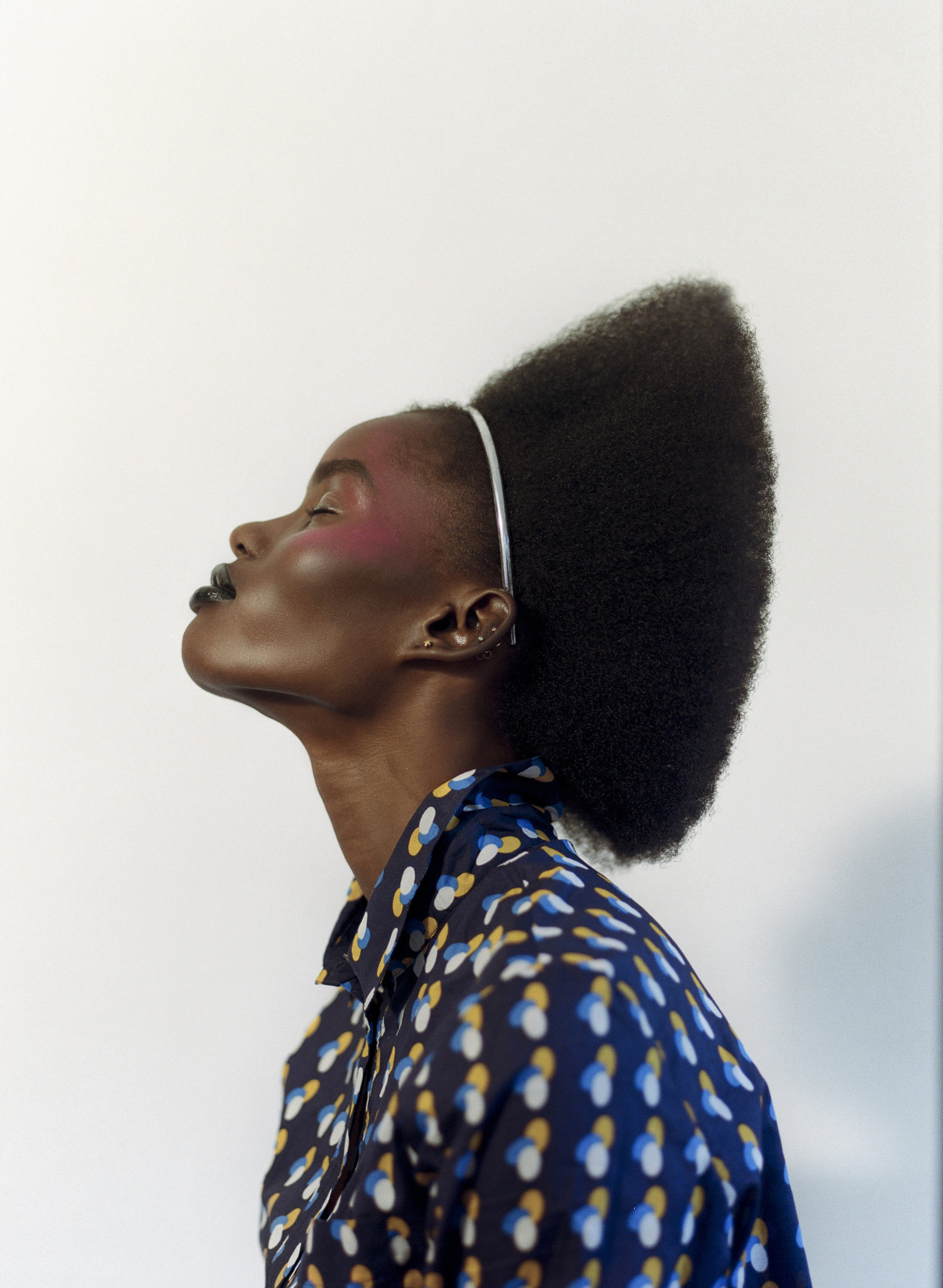 Profile shot of an African-American woman with a stylish afro and a patterned button-down shirt against a stark white background.