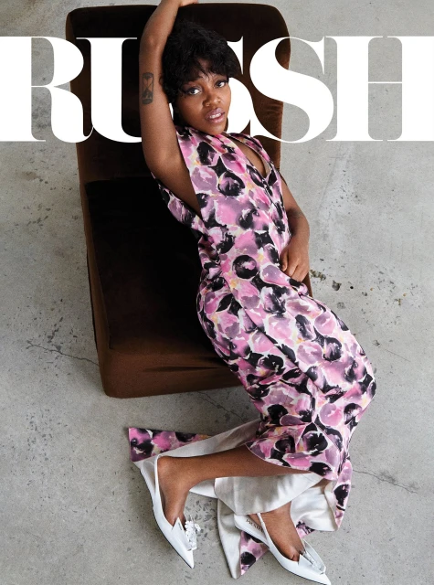 Woman in floral dress seated on chair with magazine cover in a studio setting, captured from an overhead angle.