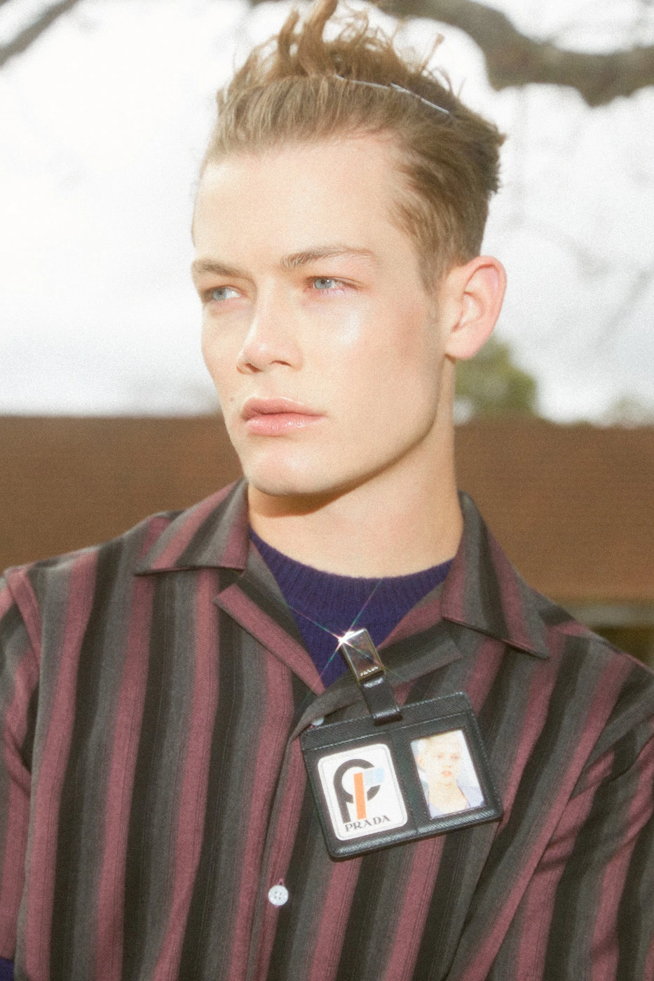 Close-up portrait of a male model wearing a striped short-sleeve shirt with an ID badge clipped to the collar.