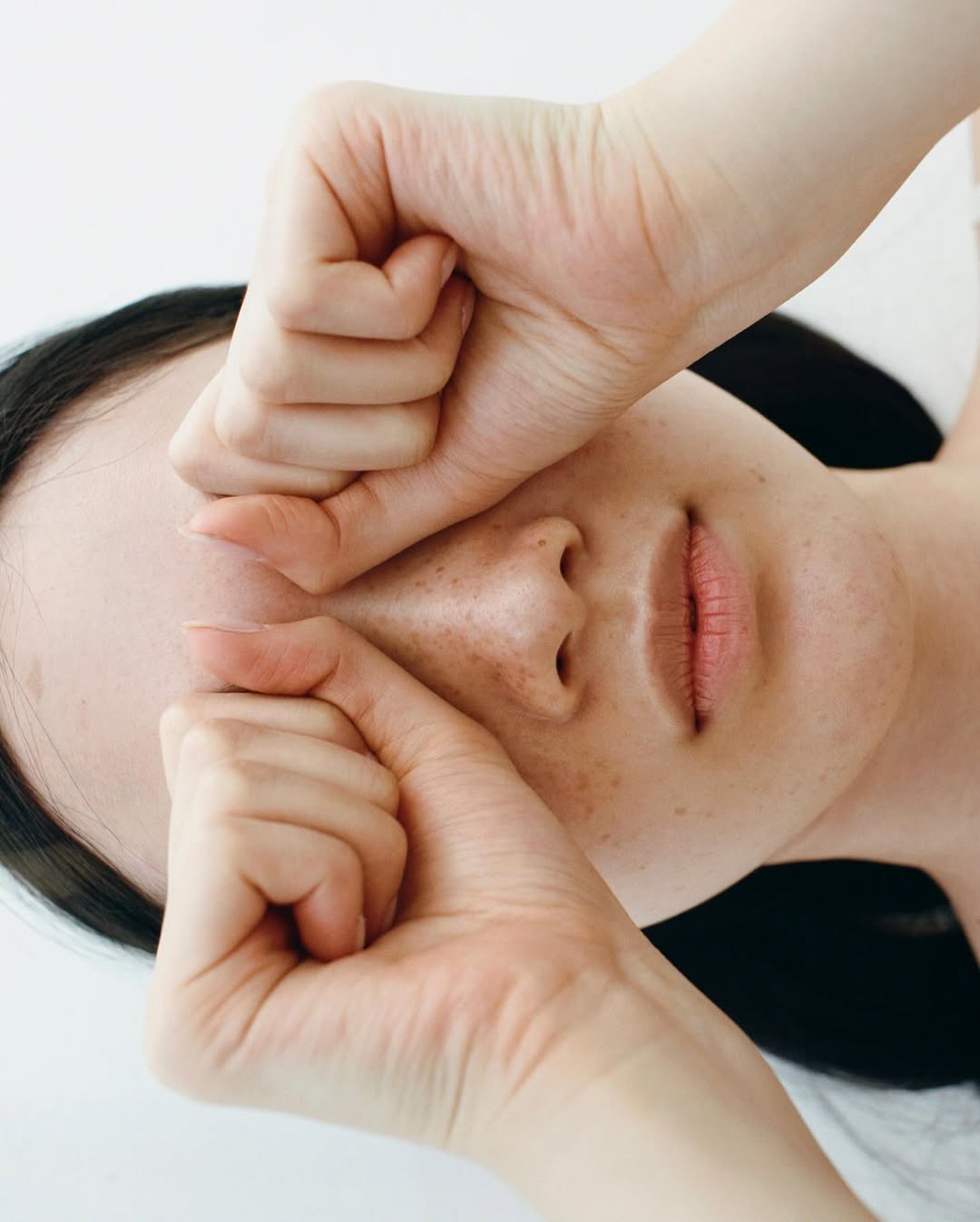 Adult woman with hands covering face against a white background in a close-up studio portrait focused on skincare and relaxation.