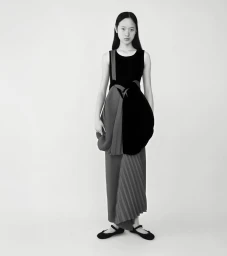 Monochrome portrait of an east asian woman standing against a plain white background wearing an avant garde pleated dress.