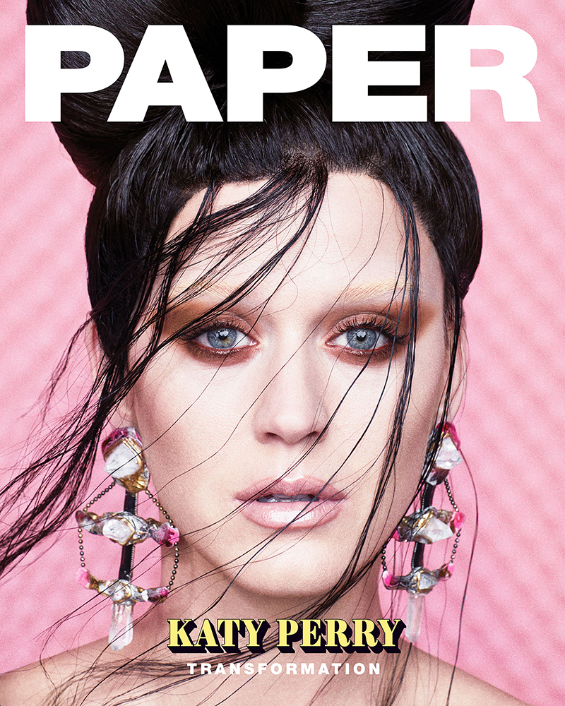 Close-up portrait of Katy Perry for Paper Magazine cover with elaborate updo hairstyle and large earrings in front of a pink background.