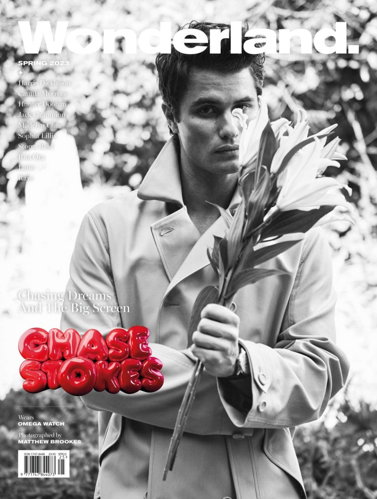 Chase Stokes covers Wonderland magazine, Spring 2023 issue. He is holding a large flower, wearing a trench coat in an outdoor setting.