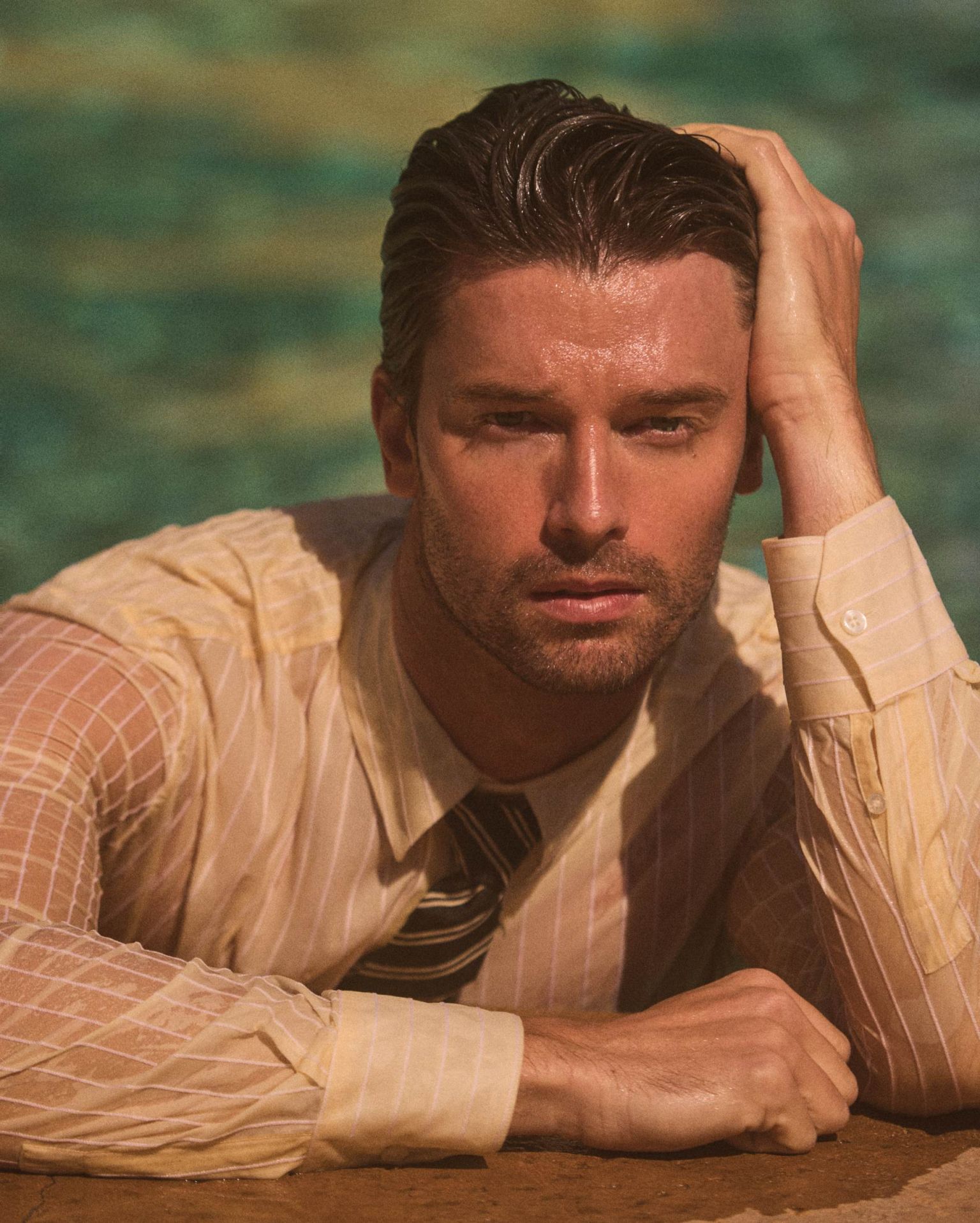 Close-up portrait of a man with wet hair and a striped shirt and tie. He rests his hand on his head while in water.