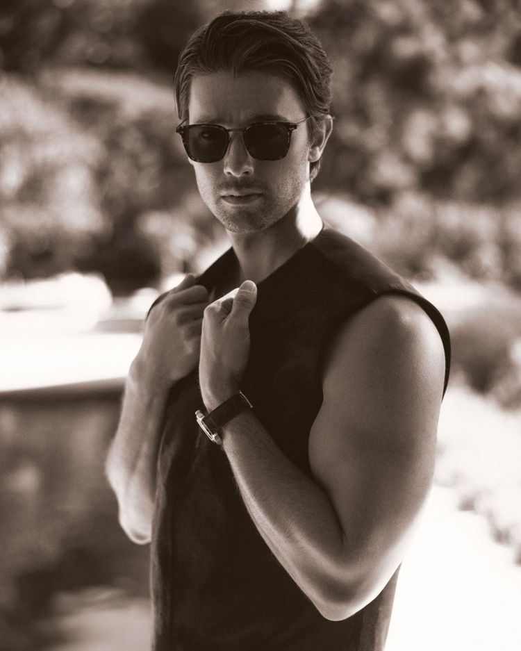 Man wearing sunglasses and a sleeveless vest, holding his collar outdoors in a portrait styled by Avo Yermagyan.