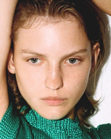 Close-up portrait of a woman with freckles wearing a green knitted sleeveless top, styled by Alberto Vegue.