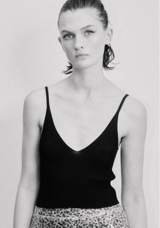 Model in a black ribbed tank top with dark winged eyeliner against a plain light background